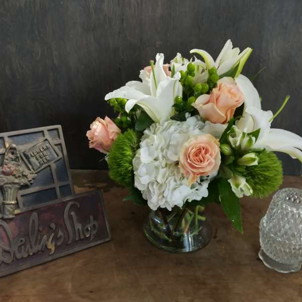 Bouquet of white lilies, peach roses, and white hydrangeas in a glass vase