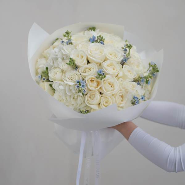 Bouquet of white roses and pale blue accents wrapped in white paper