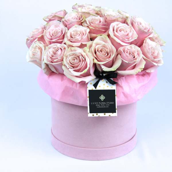 Pink roses arranged in a round hat box with a ribbon tag
