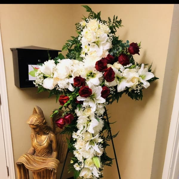 Large cross-shaped floral tribute with white lilies and red roses on a stand