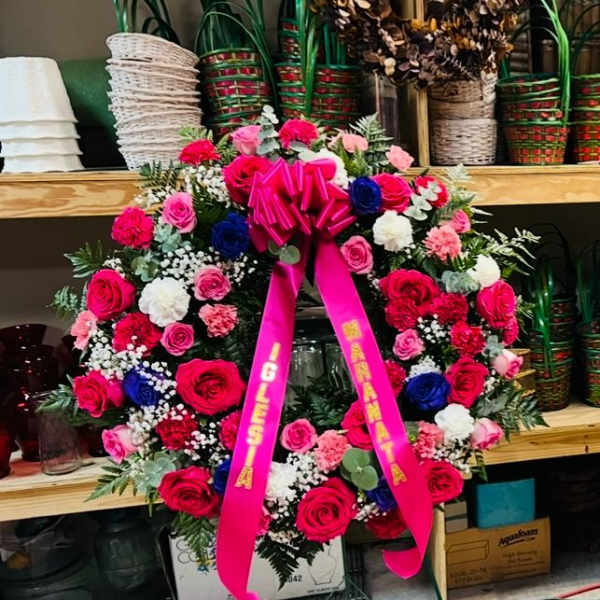 Large pink and red floral wreath on a stand with a bright ribbon