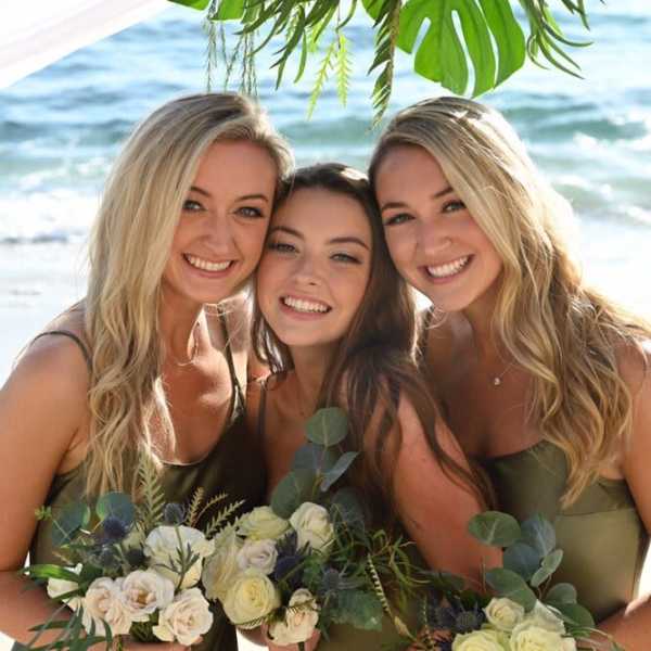 Three women holding small bouquets on a beach