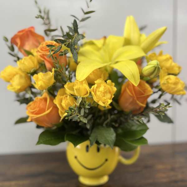 Yellow and orange flower arrangement in a smiley-face mug
