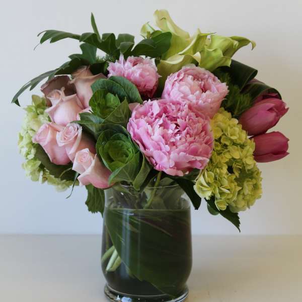Mixed arrangement of pink peonies, roses, tulips, and green hydrangeas in a clear glass vase