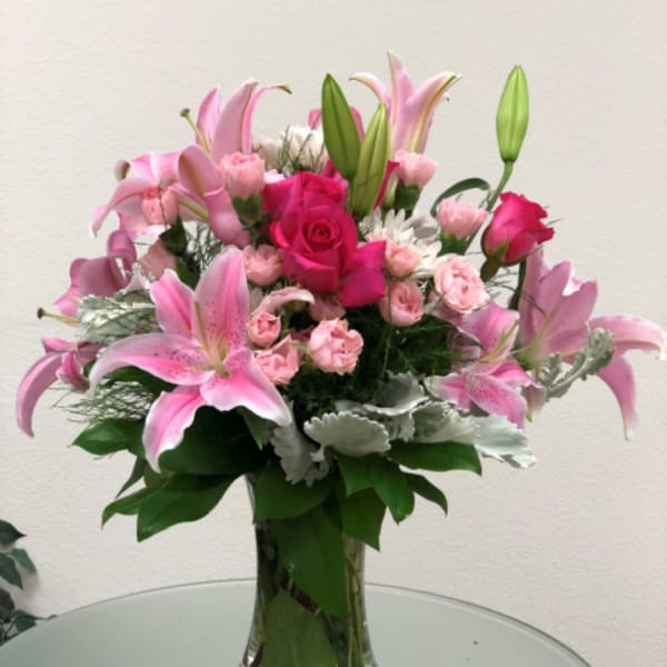 Pink lilies and roses arranged in a clear glass vase