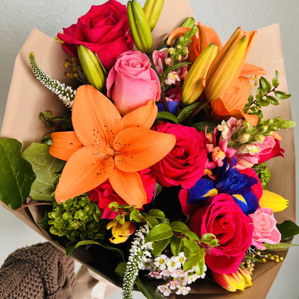 Colorful bouquet with roses, lilies, and mixed blooms wrapped in brown paper