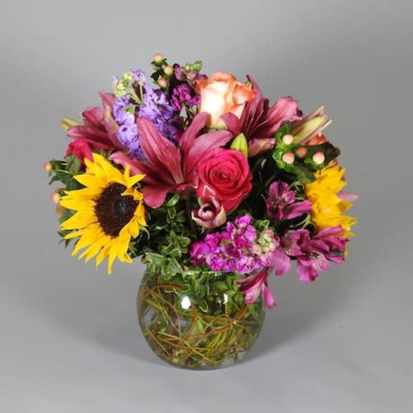 Mixed bouquet with sunflowers, roses, and lilies in a glass vase
