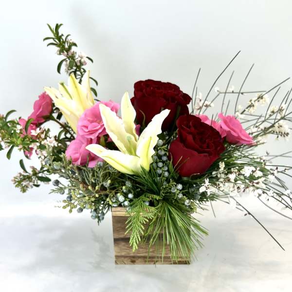 Arrangement of red and pink roses with white lilies in a wooden box