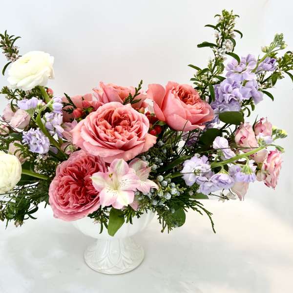 Pink and lavender roses arranged in a white pedestal vase