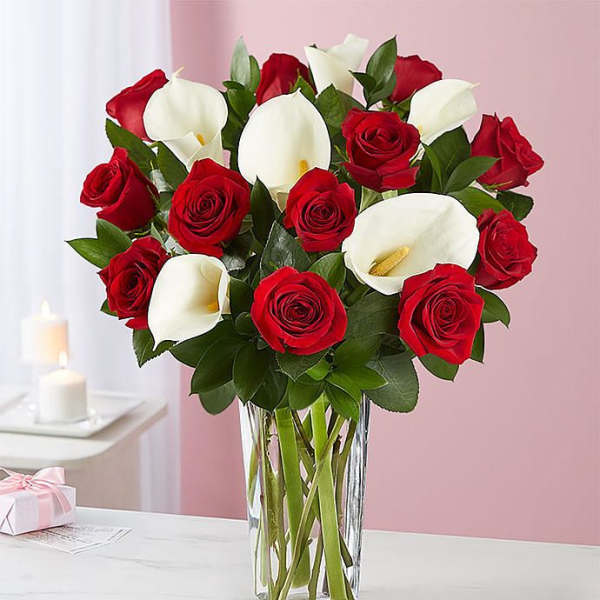 Red roses and white calla lilies arranged in a clear glass vase.
