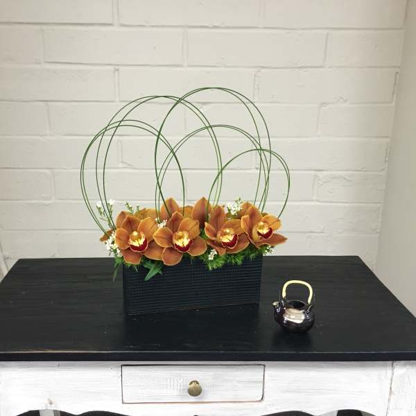 Orange orchids in a black rectangular container with green wire loops