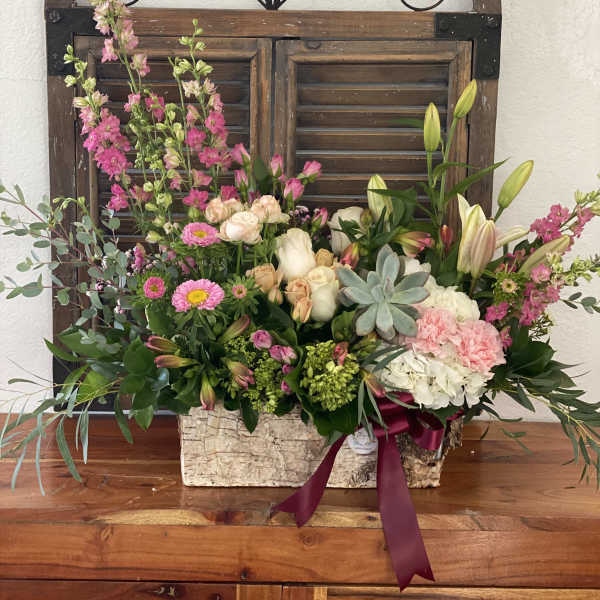 Mixed floral arrangement in a rustic rectangular container with pink and white blooms