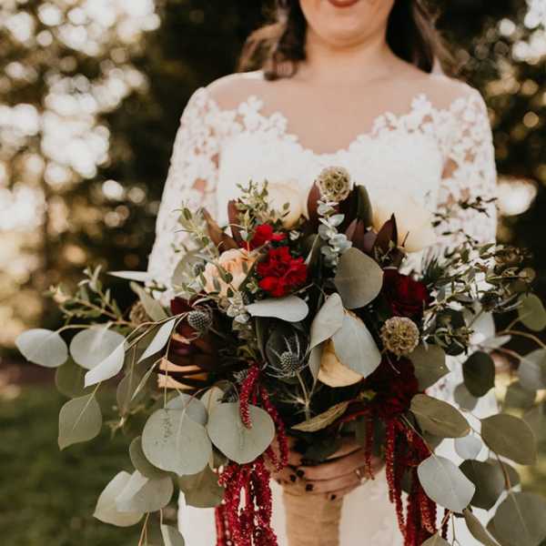 Bride holding a large bouquet with red flowers and trailing greenery
