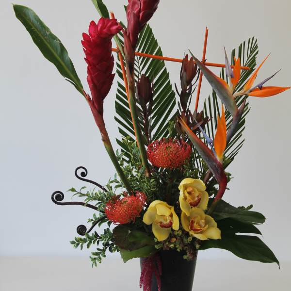 Tall tropical arrangement with red ginger, bird-of-paradise, and yellow orchids in a black vase