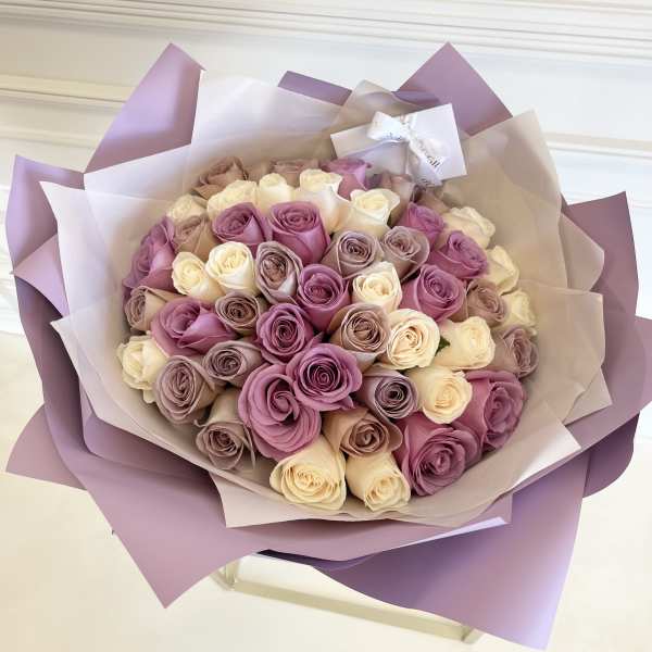 Bouquet of pink, lavender, and cream roses wrapped in purple paper