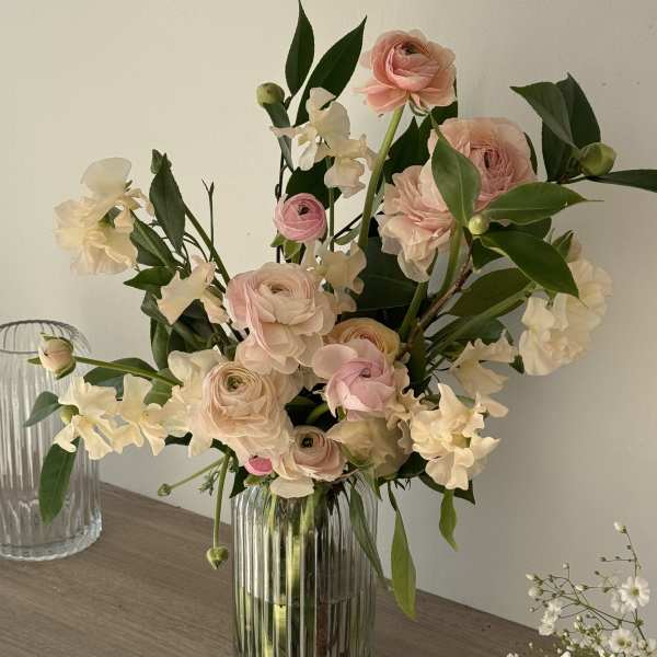 Blush pink ranunculus and white sweet pea in a clear glass vase