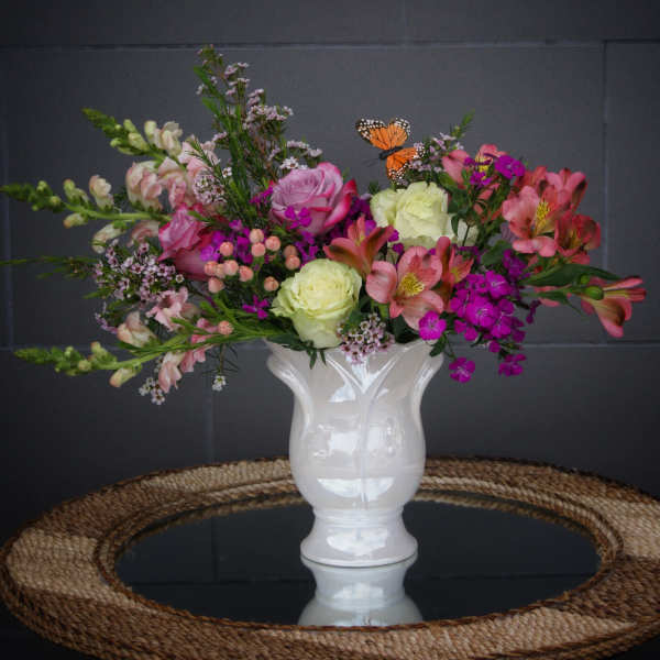 Mixed pink and white flowers in a white vase with a butterfly accent