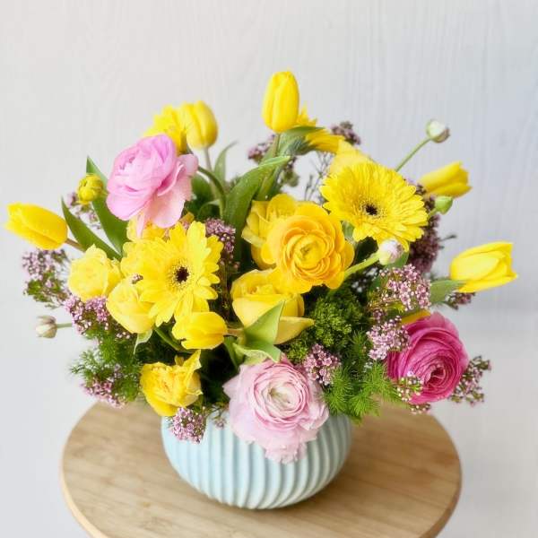Yellow and pink mixed flowers arranged in a ribbed blue vase