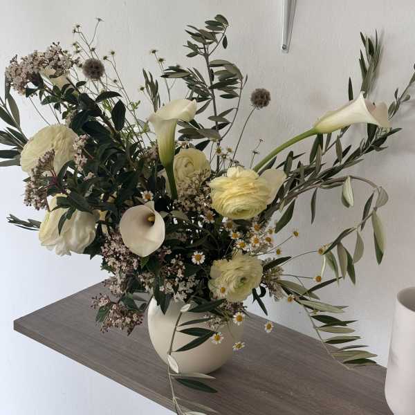 White floral arrangement in a cream vase with calla lilies and ranunculus