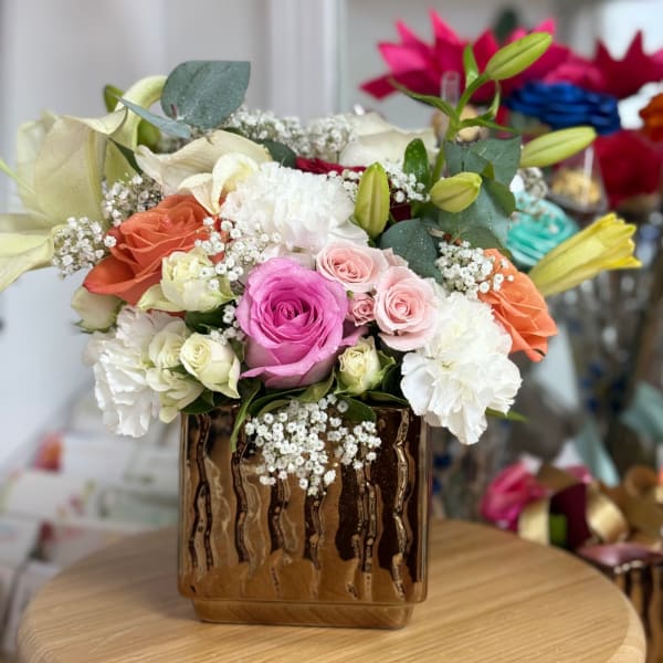 Mixed bouquet of roses, lilies, and carnations in a gold vase