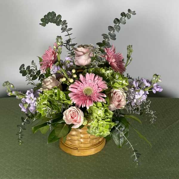 Pink gerbera daisies and roses in a woven basket with lavender accents
