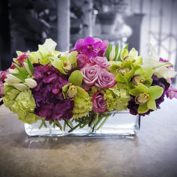 Mixed pink, purple, and green flowers arranged in a clear rectangular vase