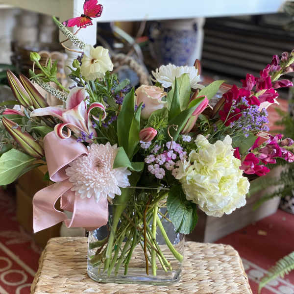 Mixed bouquet in a clear glass vase with pink ribbon and lilies