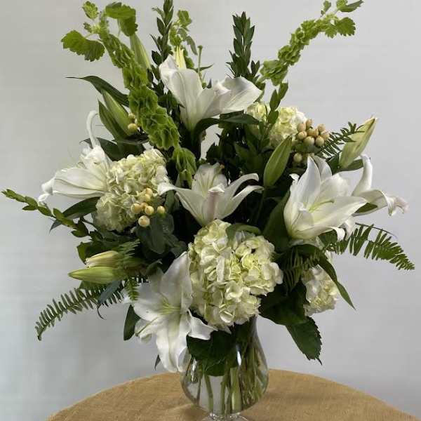 White lilies and pale hydrangeas arranged in a clear glass vase