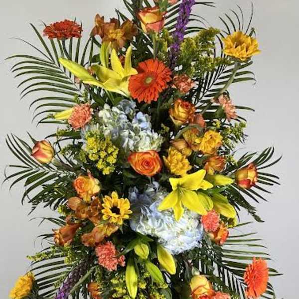 Tall standing floral spray with mixed bright flowers on a black easel