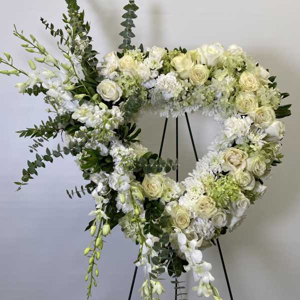 Heart-shaped white floral wreath on a black stand