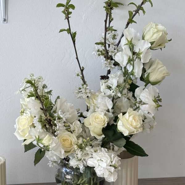 White roses and blossoms arranged in a clear glass vase