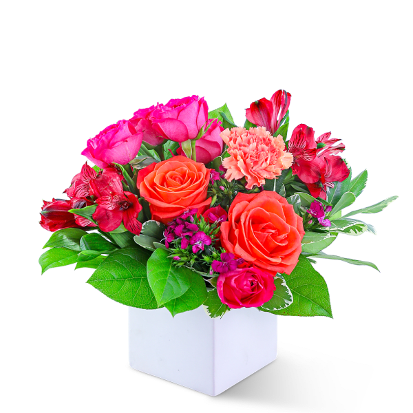 Pink and orange flower arrangement in a white cube vase