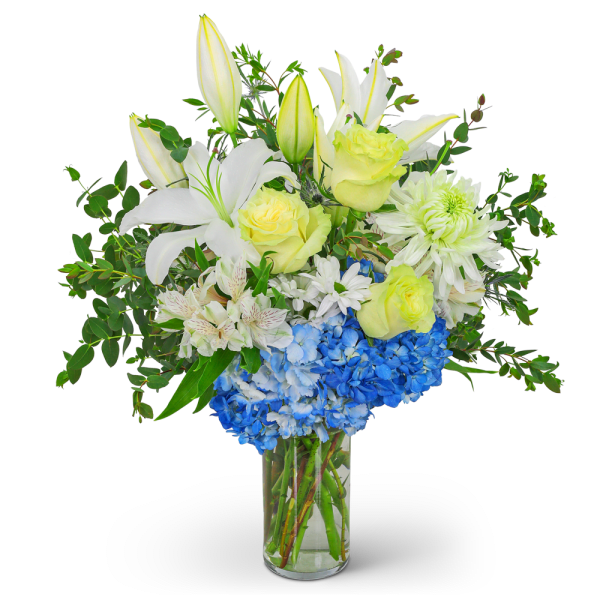 White lilies, yellow roses, and blue hydrangeas in a clear glass vase