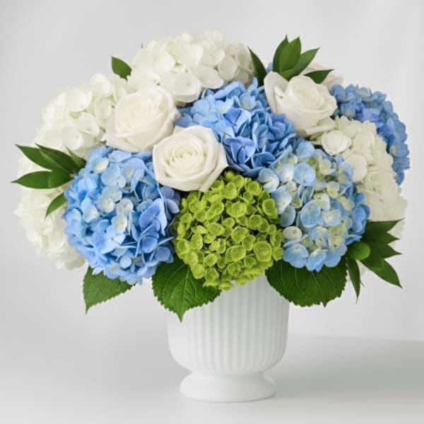 Blue and white hydrangea bouquet with white roses in a white vase