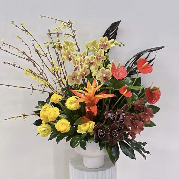 Tropical floral arrangement with orchids, anthuriums, and yellow roses in a white vase
