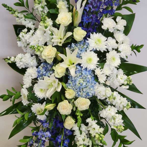 Tall white and blue standing spray with lilies, roses, hydrangeas, and mums on a metal easel