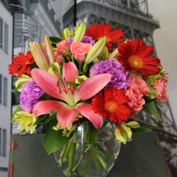 Mixed bouquet of pink lilies, red gerbera daisies and purple carnations in a clear glass vase