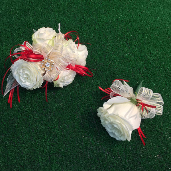 Two white rose corsages with red and gold ribbon accents