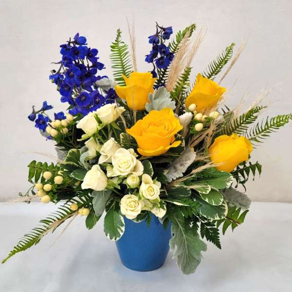 Bouquet of yellow and white roses with blue flowers in a blue vase