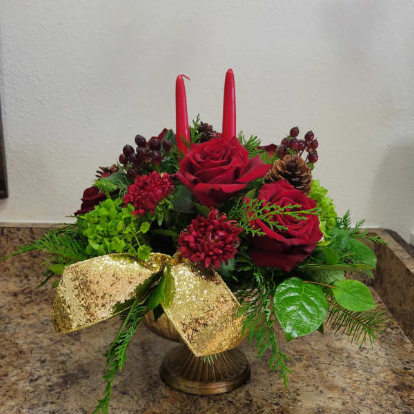 Low red and green holiday centerpiece with roses, candles, pinecones and a gold bow in a pedestal bowl