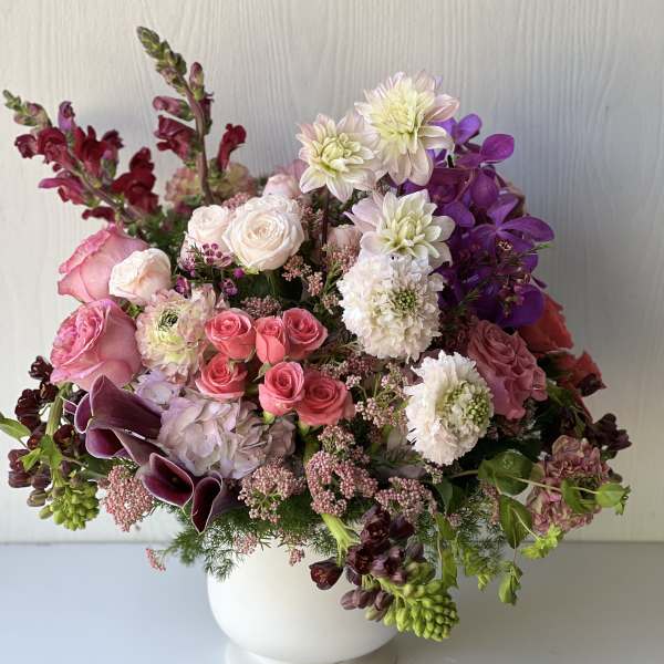 Mixed pink, white, and purple flowers arranged in a white vase