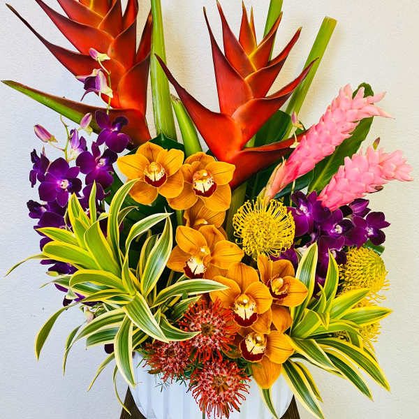 Tropical arrangement with orange heliconia, orchids, and pink ginger in a white vase