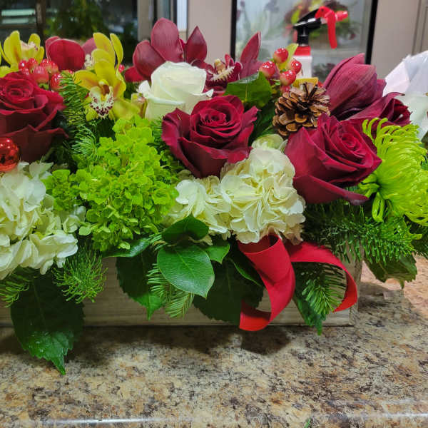 Rectangular holiday centerpiece with red roses, white hydrangeas, green mums, orchids, and evergreens in a wooden box.