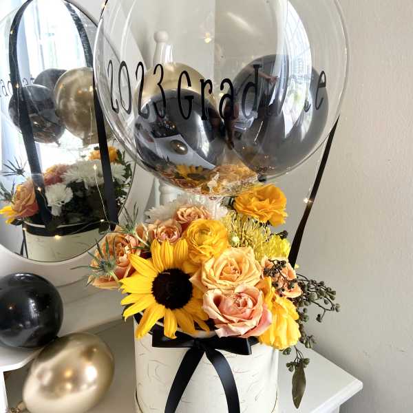 Graduation balloon arrangement with yellow and peach flowers in a hatbox