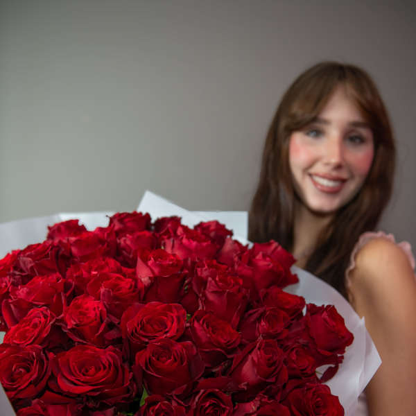 Woman holding a large bouquet of red roses wrapped in white paper