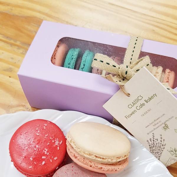 Assorted macarons on a white plate beside a lavender gift box with ribboned tag