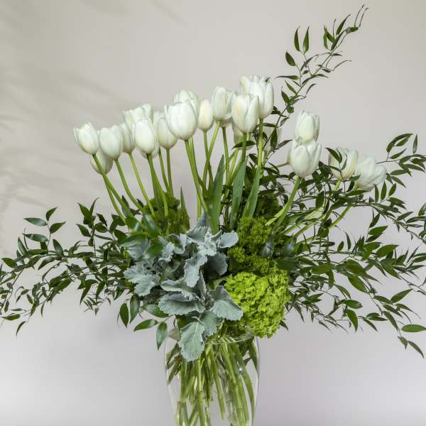 White tulips in a clear glass vase with mixed greenery