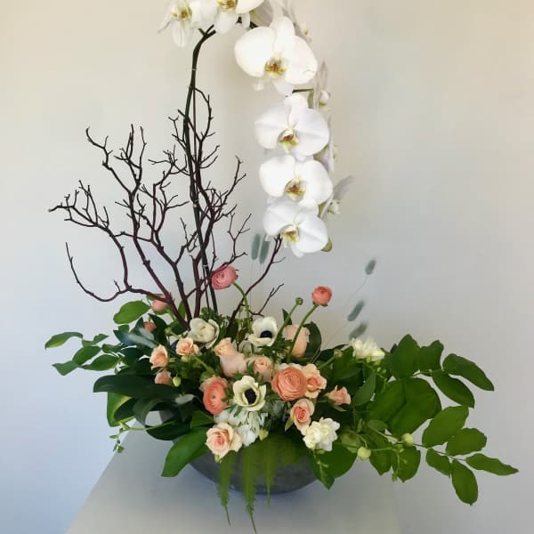 White orchid arrangement with peach roses in a low bowl
