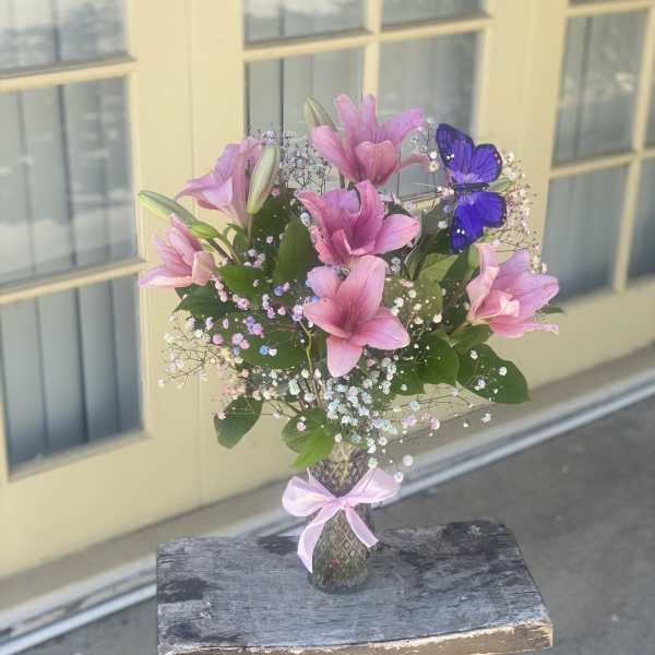 Pink lilies in a glass vase with a purple butterfly decoration