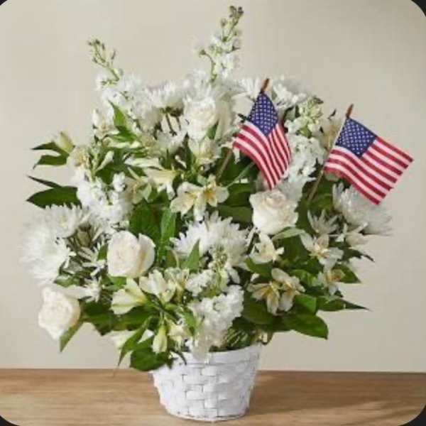 White floral arrangement in a white basket with two small American flags